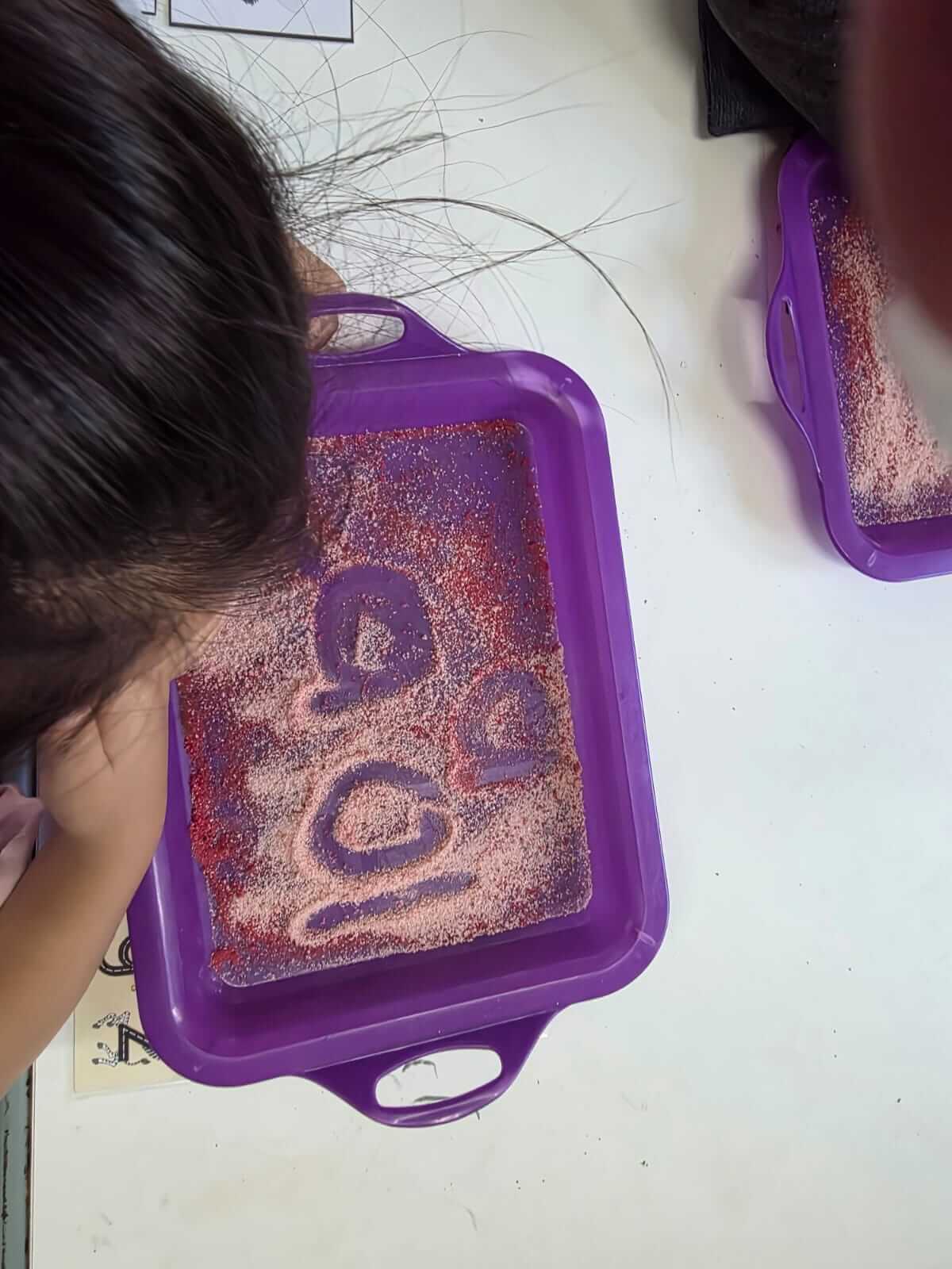 Sensory writing activity at Petra Christian Pre-School — a child tracing letter shapes with their finger in a purple tray filled with jelly