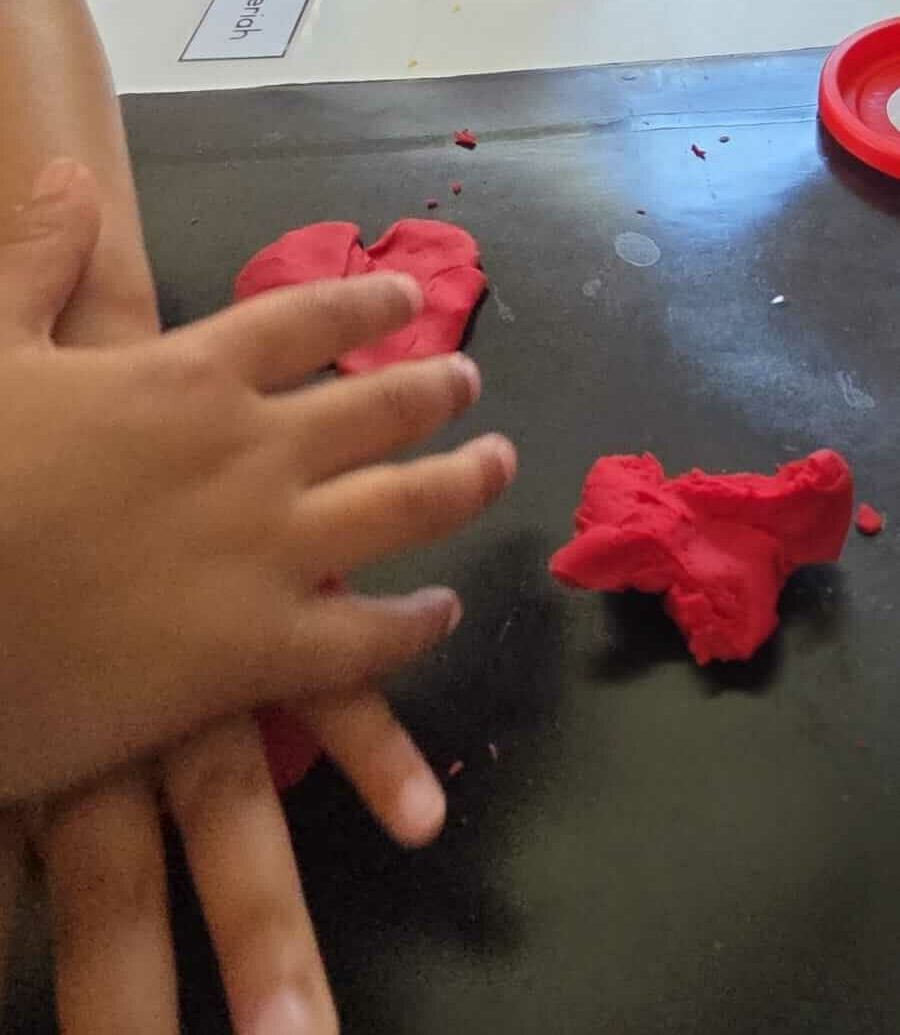 Playdough sensory activity at Petra Christian Pre-School — a child's hands moulding and shaping red playdough