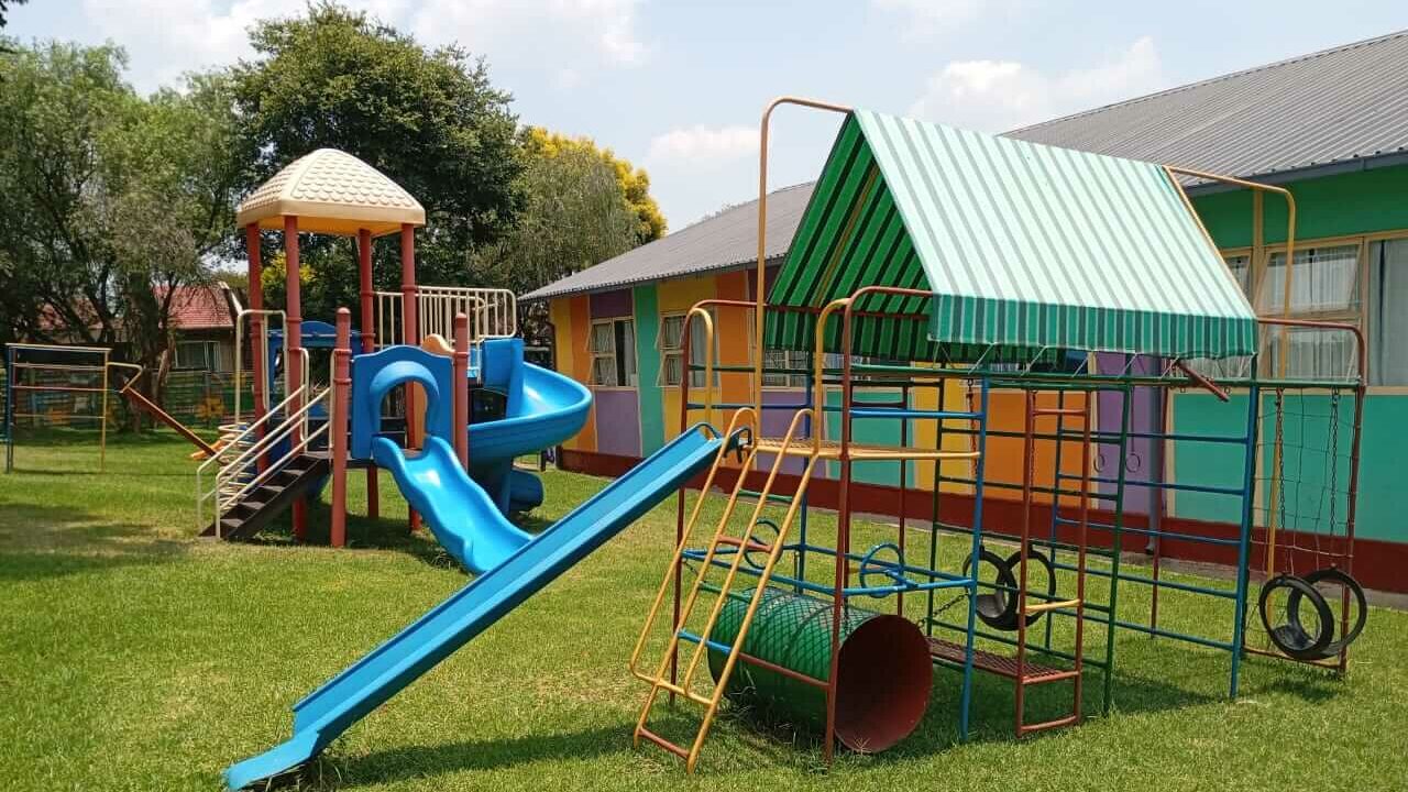Alt Text Outdoor playground at Petra Christian Pre-School, Edenvale, Johannesburg — featuring colourful jungle gyms, a blue slide, climbing frames with tyres and a crawl tunnel, a shaded play structure with shaded canopy